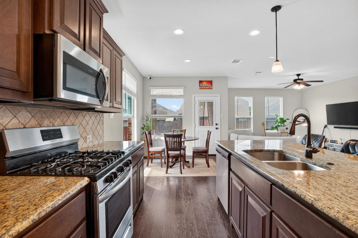 Professional real estate kitchen photo with stainless steel appliances, granite countertops, and warm natural light