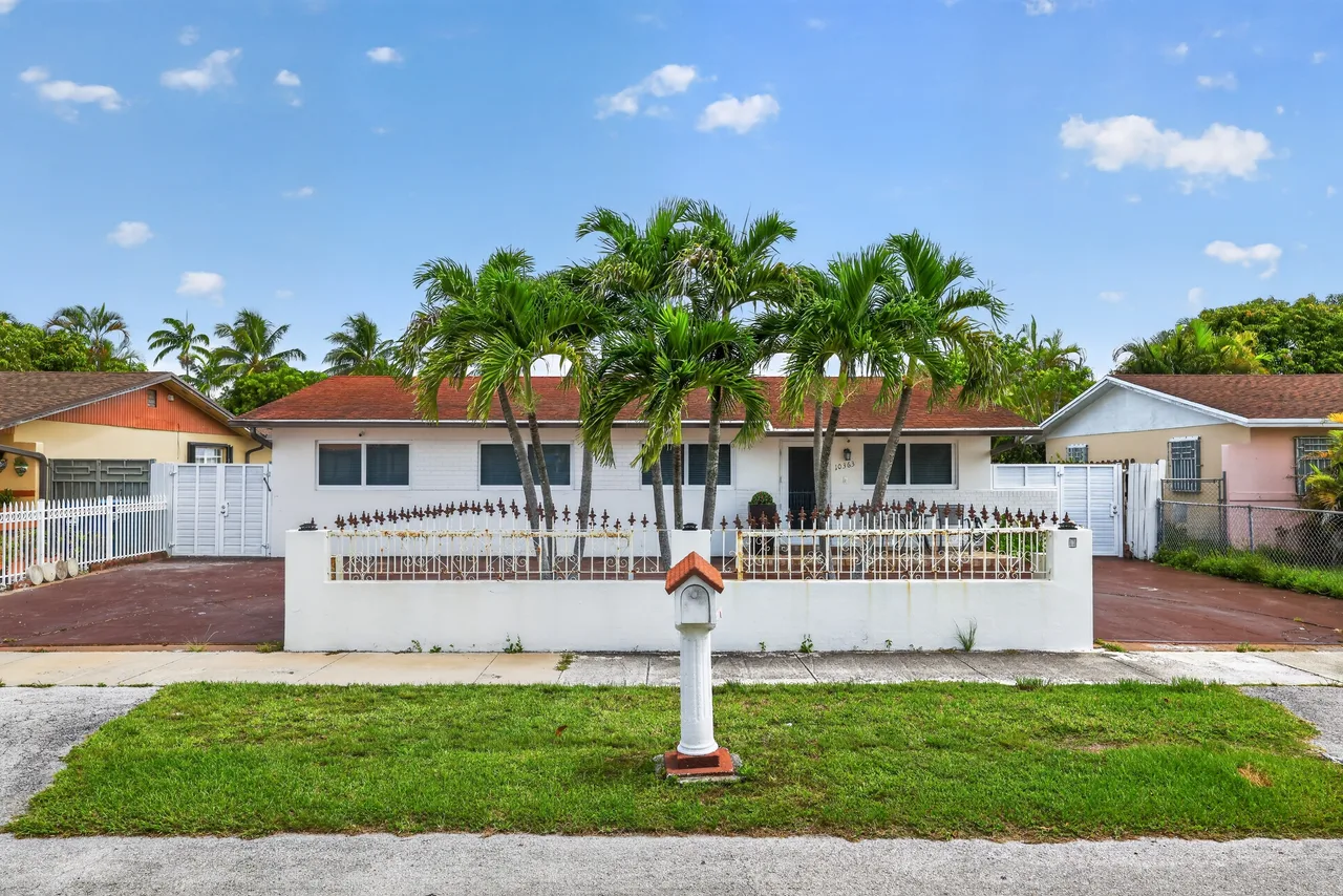Single-story home exterior framed by palm trees, photographed straight-on to accurately represent the property's true scale
