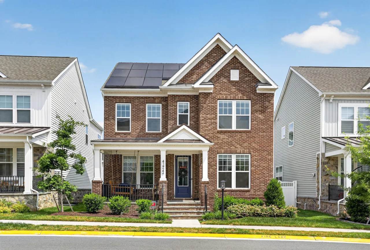 Brick two-story home with a covered front porch and solar panels on a tree-lined street