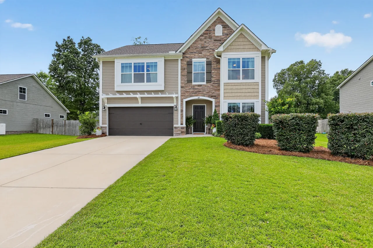 Two-story stone and siding home with a freshly mowed lawn, trimmed hedges and new mulch beds