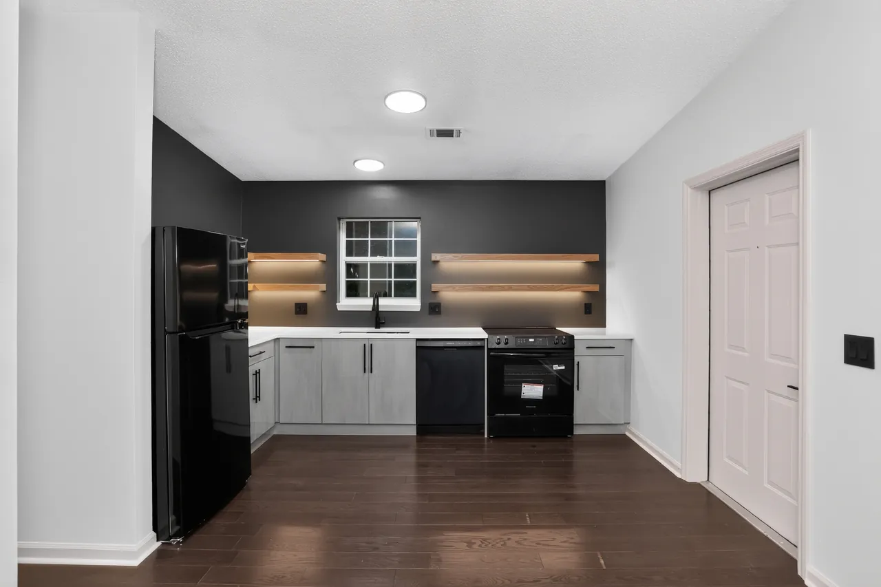 Refreshed kitchen with gray flat-panel cabinets, lit floating wood shelves, a dark accent wall and new appliances