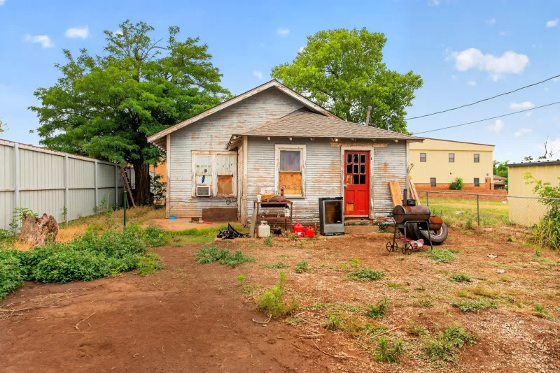 A distressed, boarded-up vacant house with a red front door