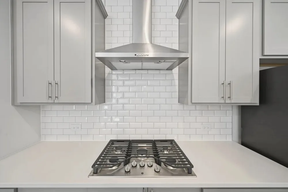 Close-up of a kitchen range hood and gas cooktop with a subway tile backsplash in a home prepared for sale