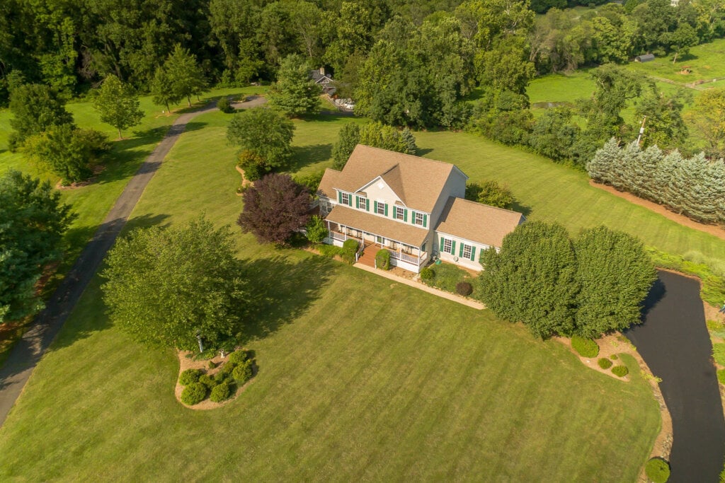 Arial show of a two story home on a large property surrounded by trees and grass. - HomeJab