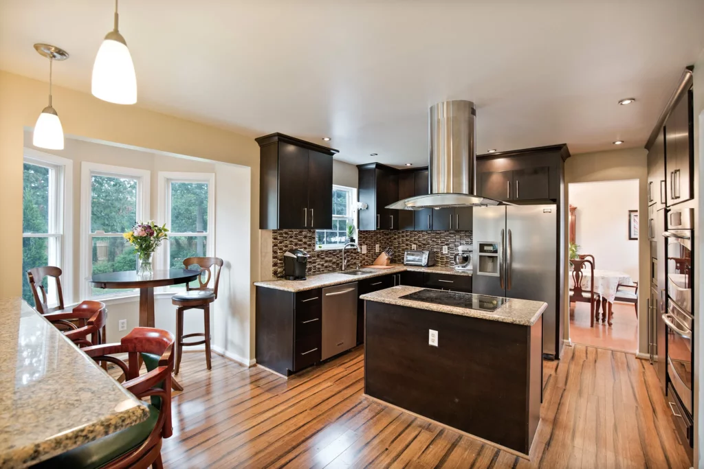 Large kitchen with black gloss cupboards and stainless steel appliances with a wood floor.  
