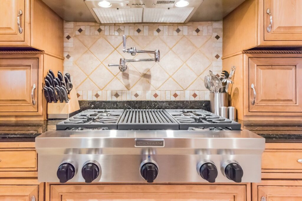Real estate photo of a professional cook top with a pot fill on the back wall.