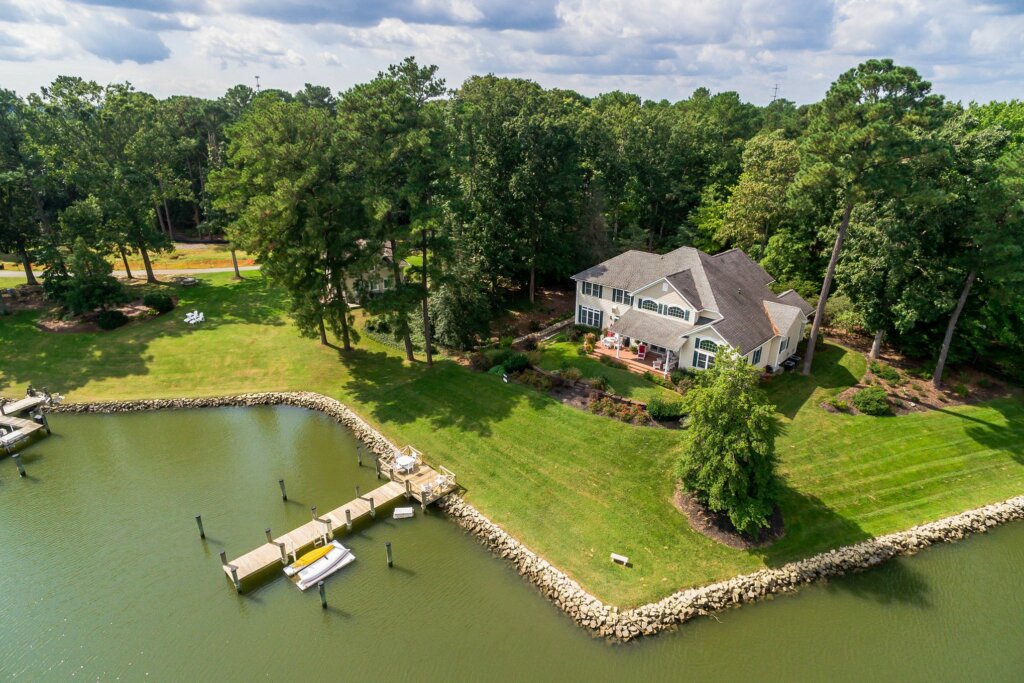 White two story home on the side of a lake with a dock. - HomeJab