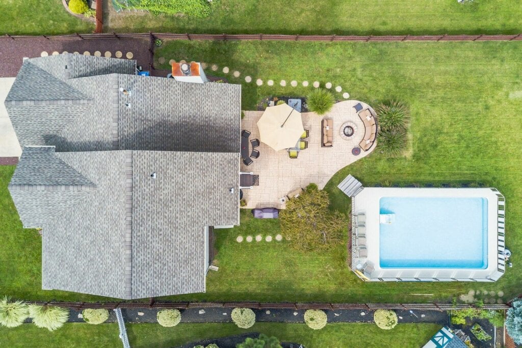 Areal drone photo of a large house with lots of grass and a pool.