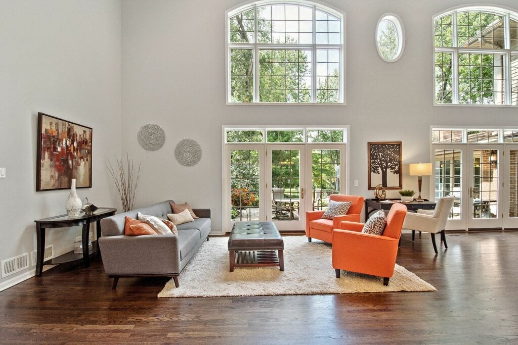 Large living room with white walls, wood floor, large windows beige rug. 