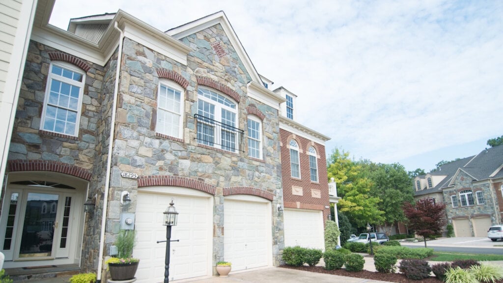 Out door photo of a large stone house with a two car garage and red brick trim.