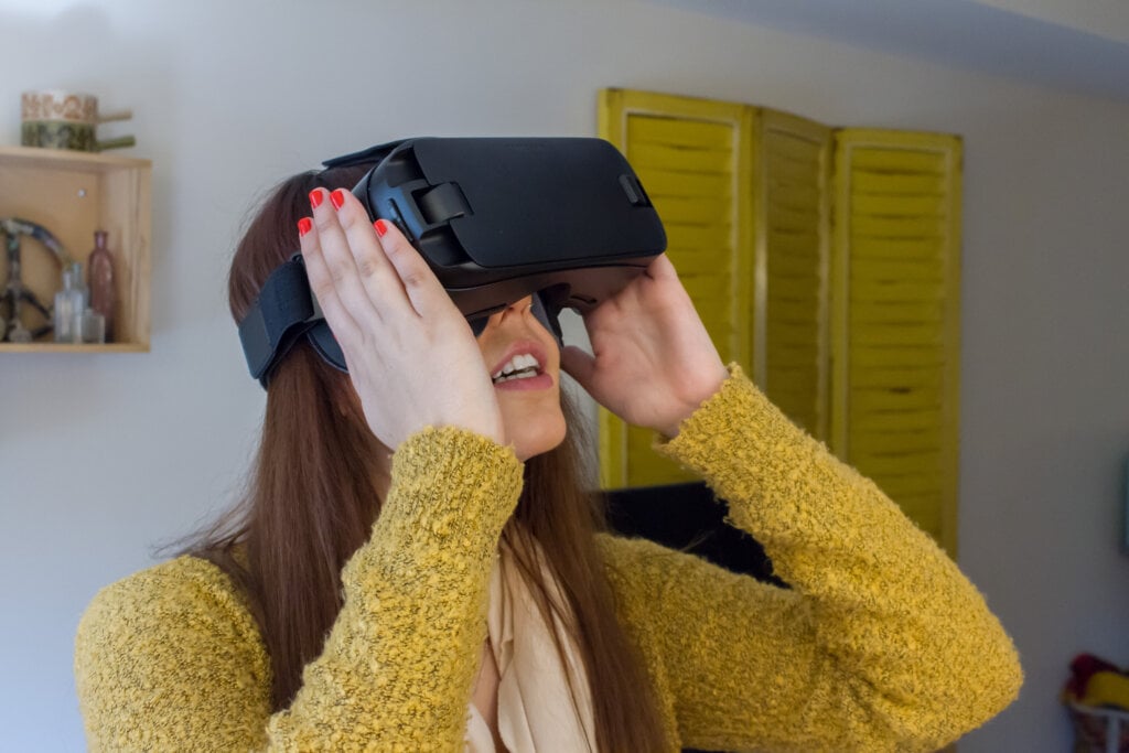 Young woman in a yellow cardigan looking through a pair of virtual reality googles.