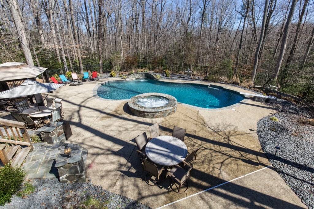 Out door photograph of a large back yard with a pool, hot tub and seating area.