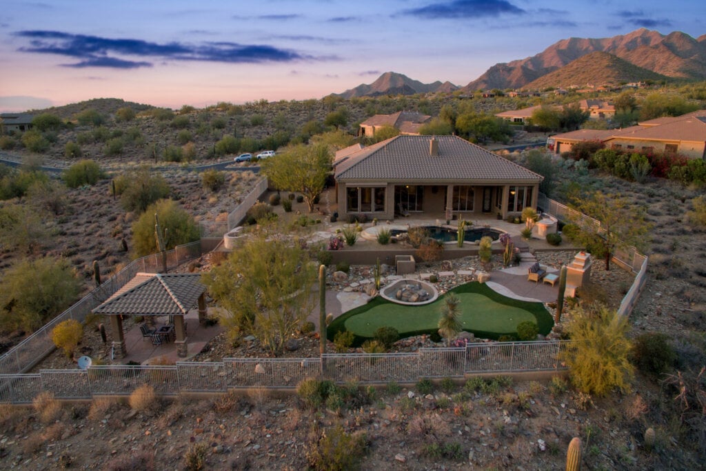 Distanced drone photo of a rustic dessert home with a large backyard and pool.