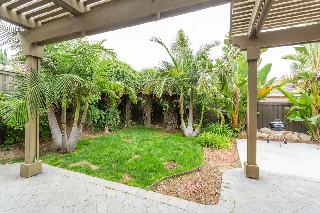 Outdoor photo of a covered brick patio facing a patch of grass with small palm trees.