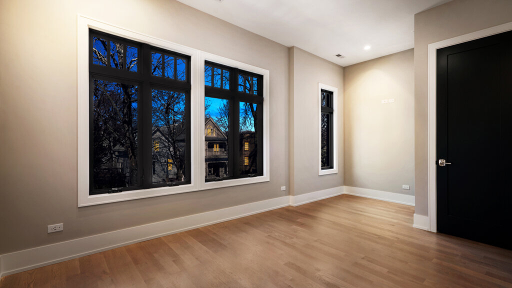 Empty room with beige walls, wood floor and large window taken at twilight.