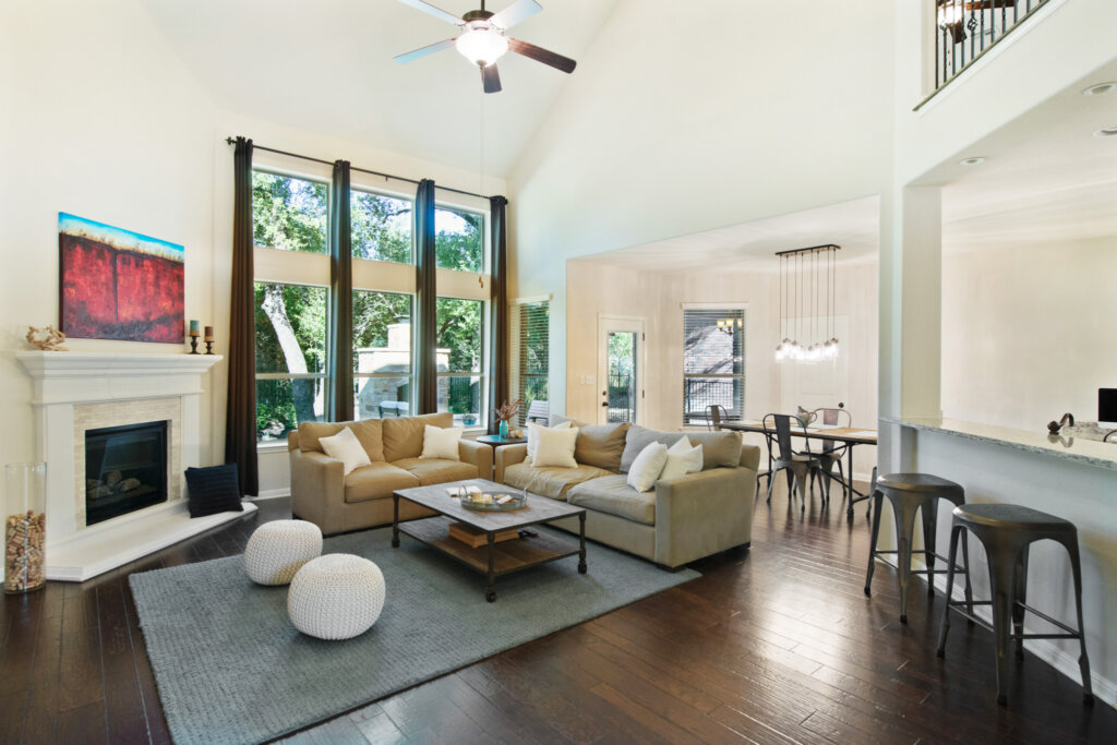 Large living room with white walls, wood floor, fireplace and tall ceiling. - HomeJab