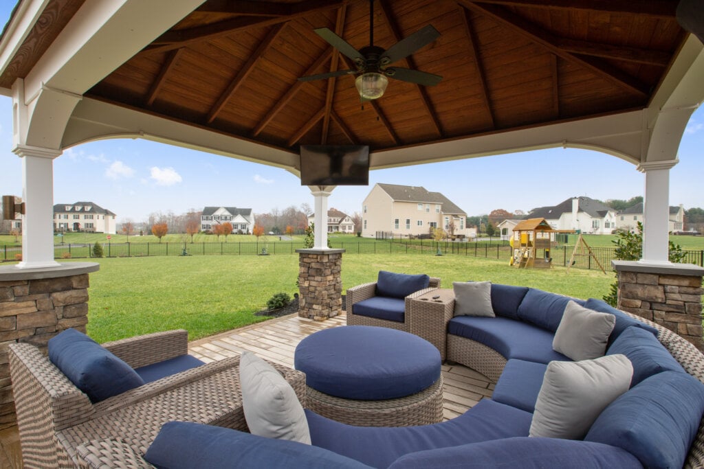 Real estate photo of a back yard with a large wicker sofa under an gazebo.