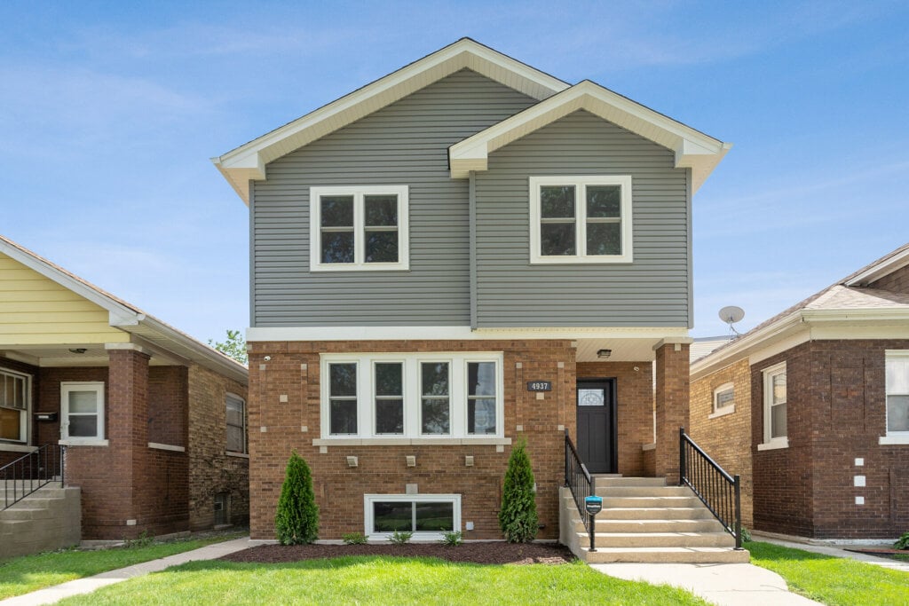 Curbside photo of two story home with half paneling and half brick.