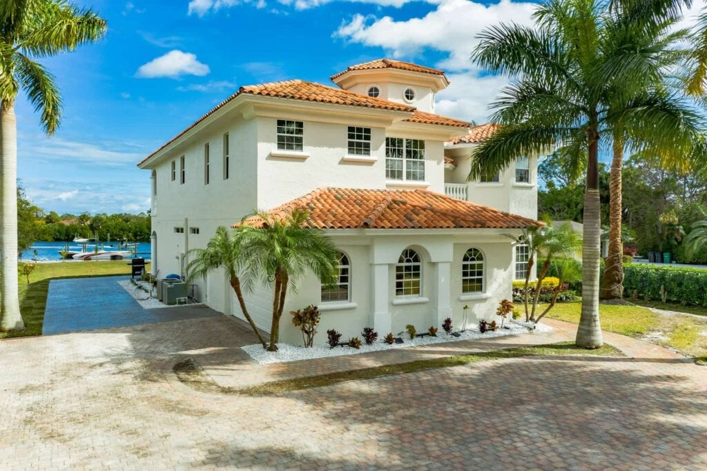 Large home with a river in the back and tiled driveway.