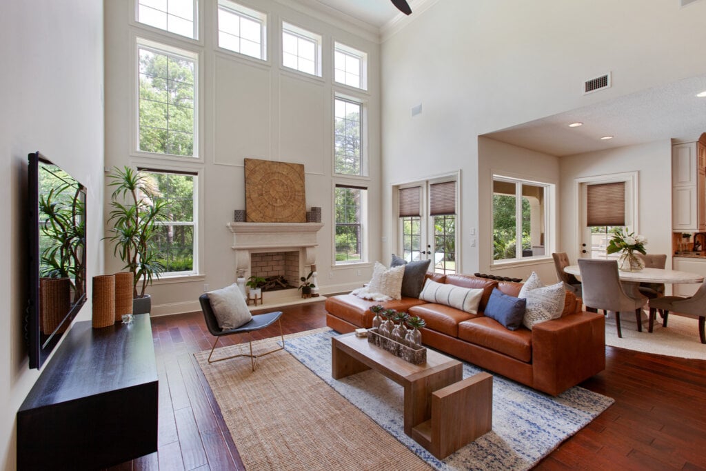 Large living room with high ceiling, picture windows, white walls and wood floor.