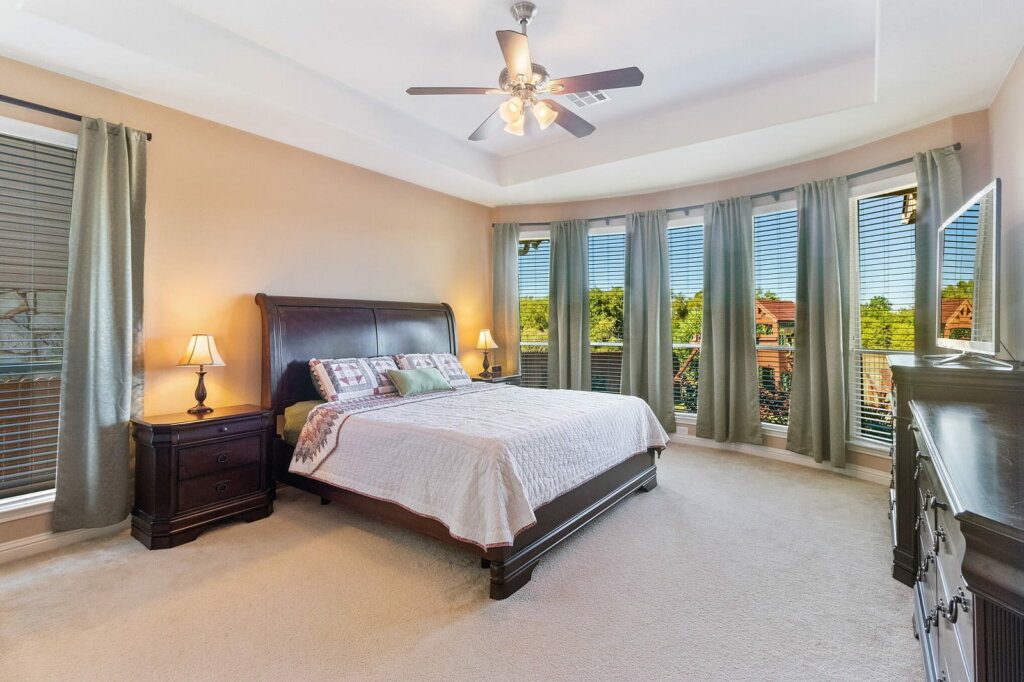 Bedroom photo showing a bed, ceiling fan and large open curtained windows.