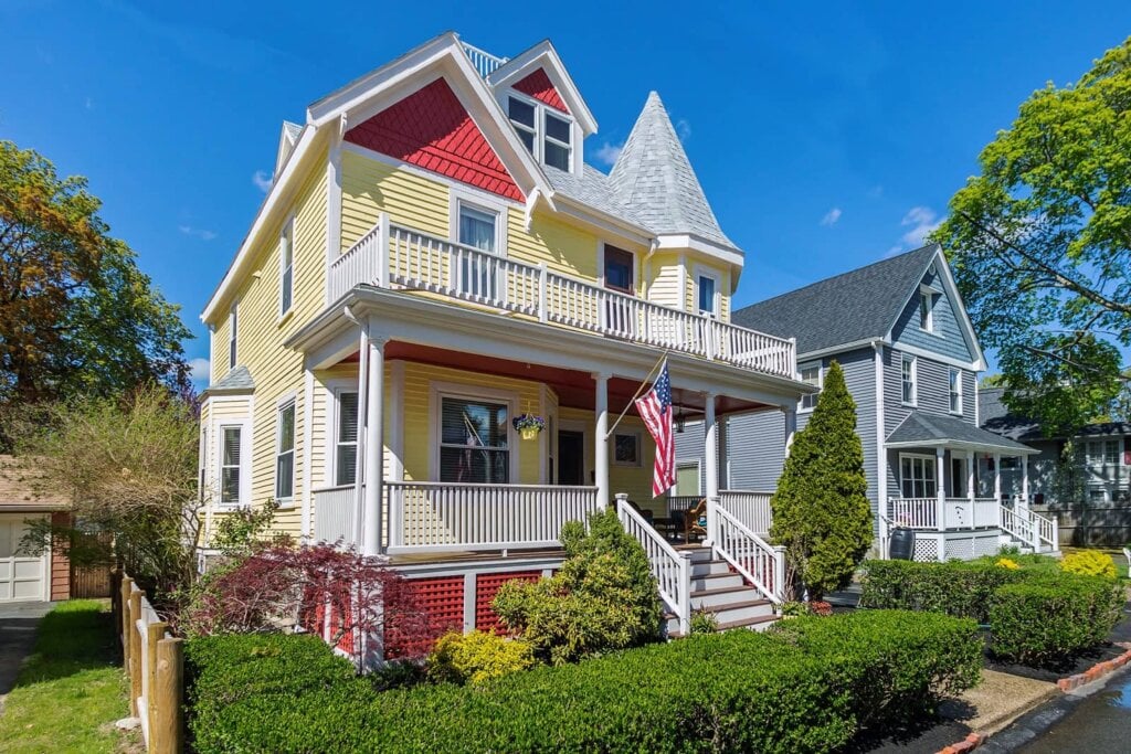 Curbside photo of a large two story home with yellow paneling and red accents.