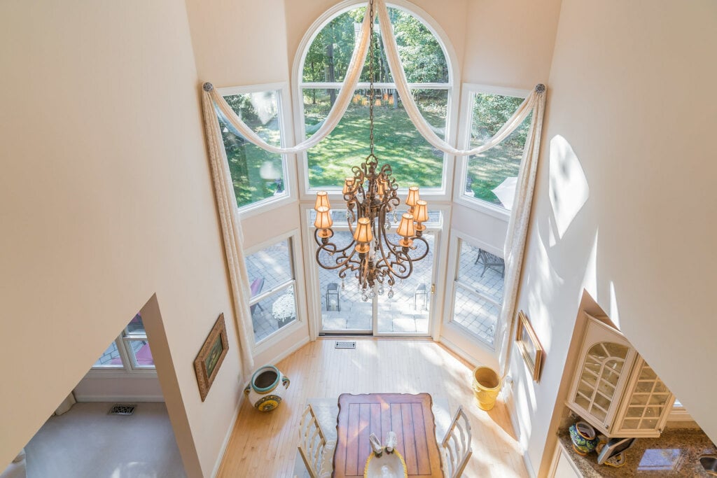 Photo look down upon a dining room area with a large set of windows and chandelier.