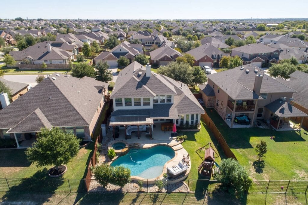 Areal drone photograph of a two story home with a large backyard and pool.