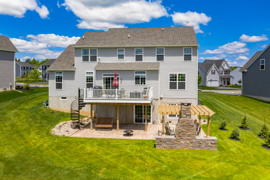 Backyard of a large 3 story home with gray siding and big yard. 