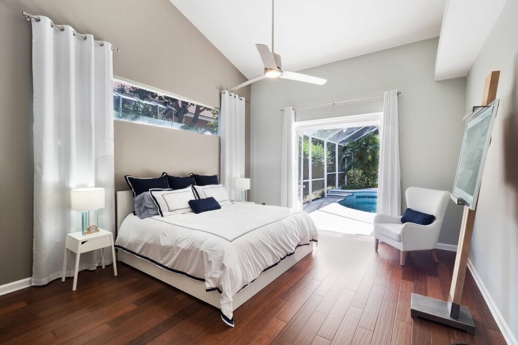 Airy bedroom with tall white curtains and wood floor and open doors leading outside.