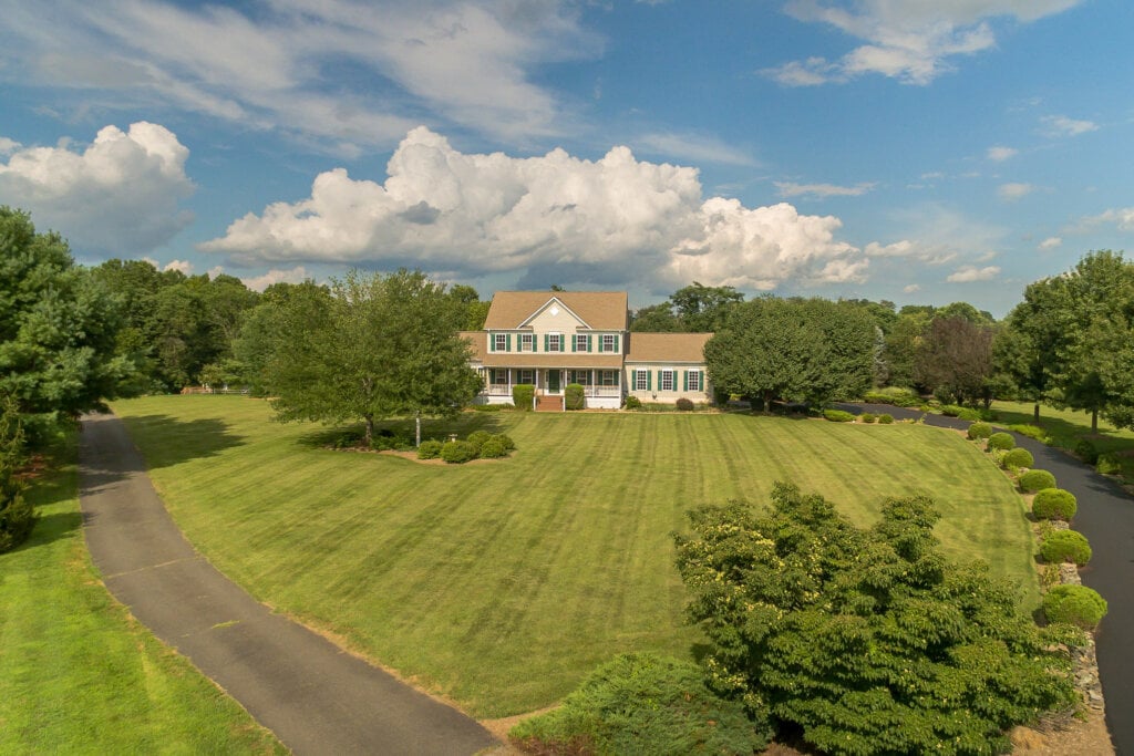 Long distance photograph of a two story house on a large property filled with trees and grass.
