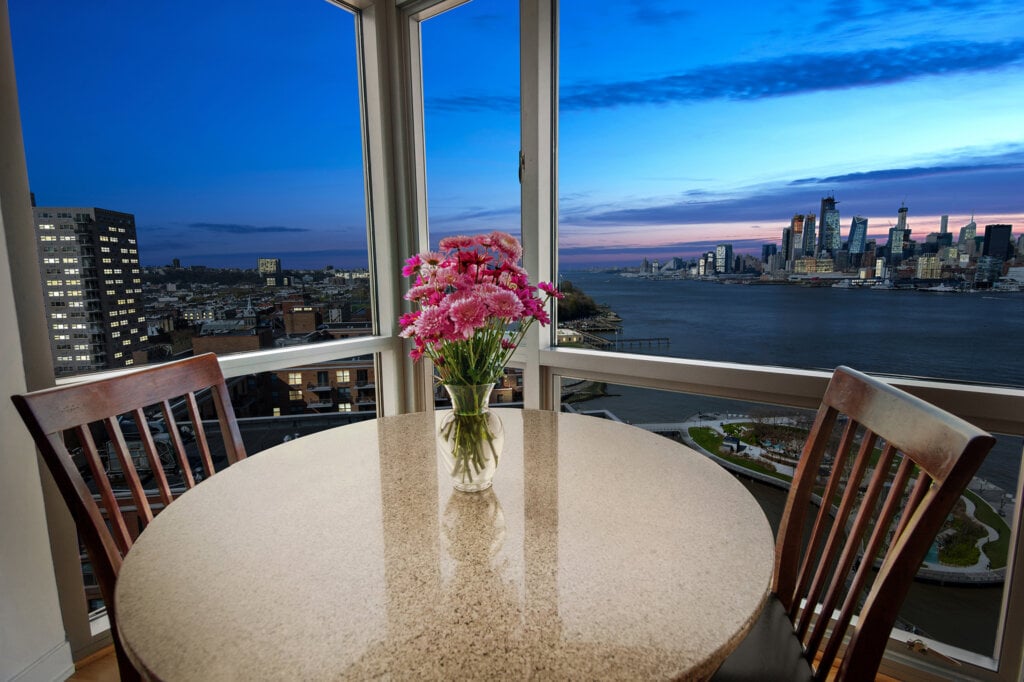 Dining table for two next to a window over looking a city next to a river.