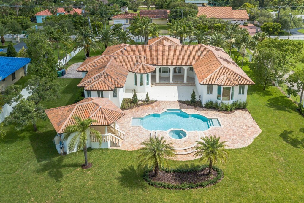 Areal drone photograph of a large white villa with a large yard and pool.