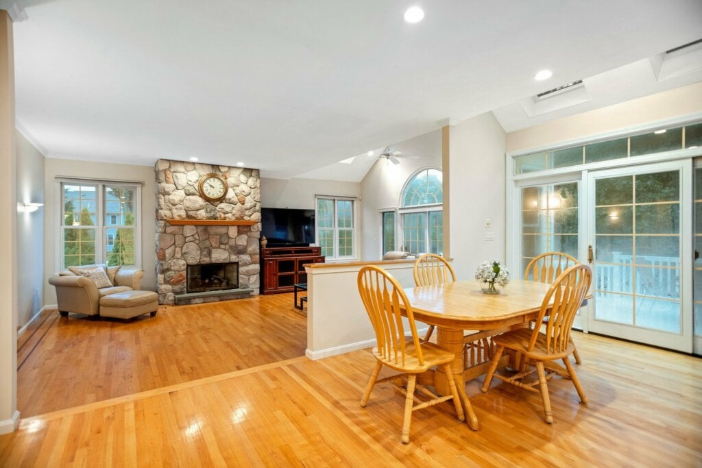 Open living and dining room area with wood floors and stone fireplace. - HomeJab