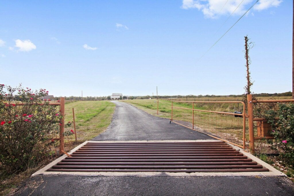Photo of a long driveway with an open metal gate leading to a home at the end.