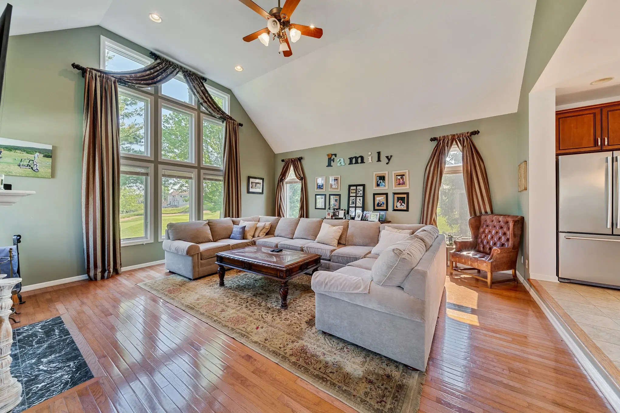 Large family room with high ceiling, wood floor and green walls with a large sofa and in the center.