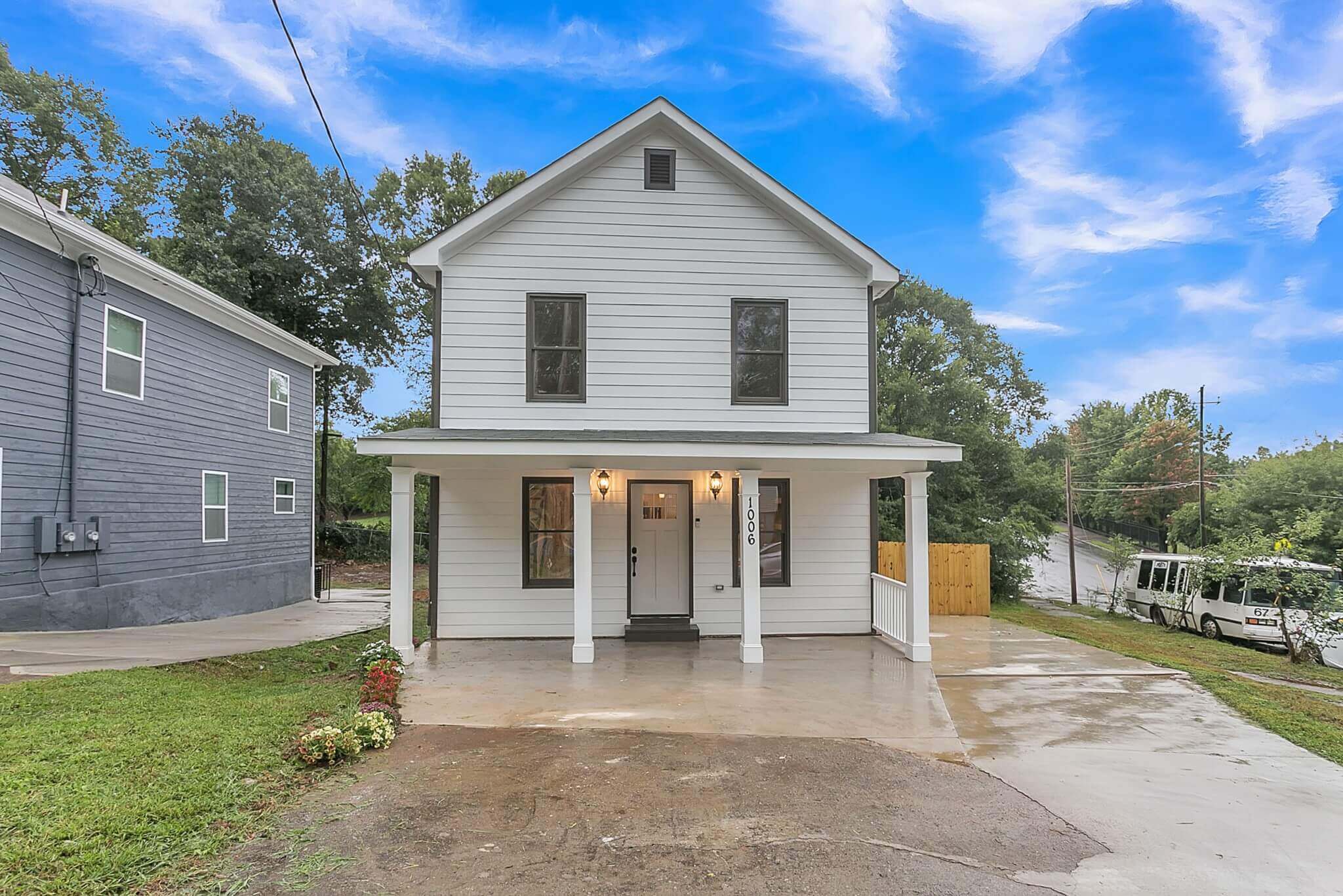 Photo of a small 2 story home painted white with a concrete patio under a blue sky.