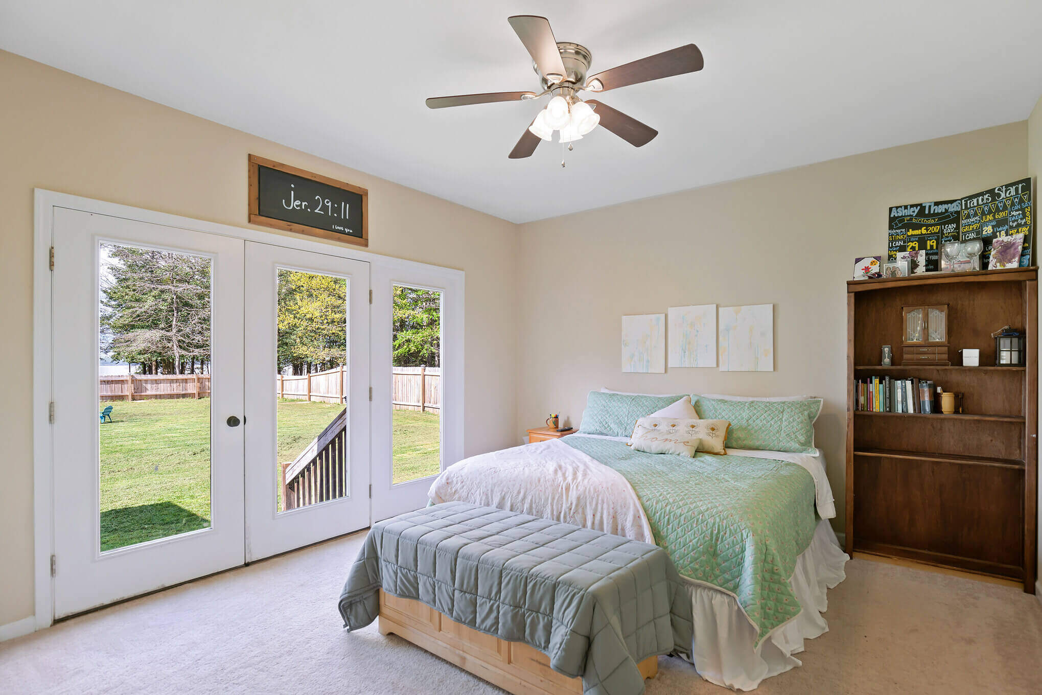 Real estate photography showing a bed room with cream colored wall. ceiling fan and patio door.