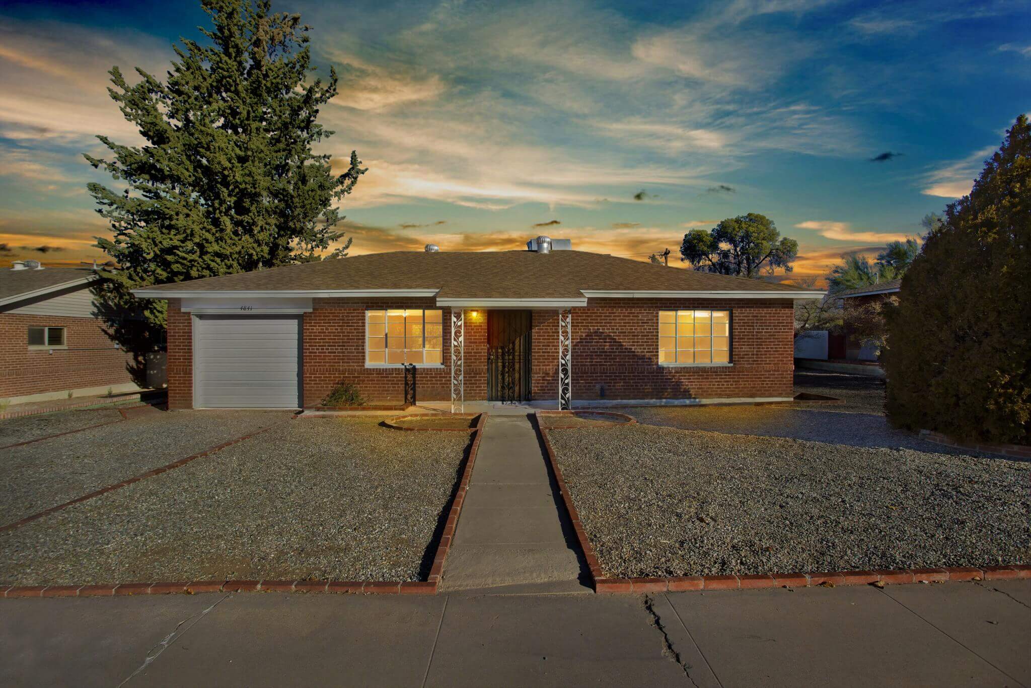 Brick home at sunset with rock lawn and two windows at street level.