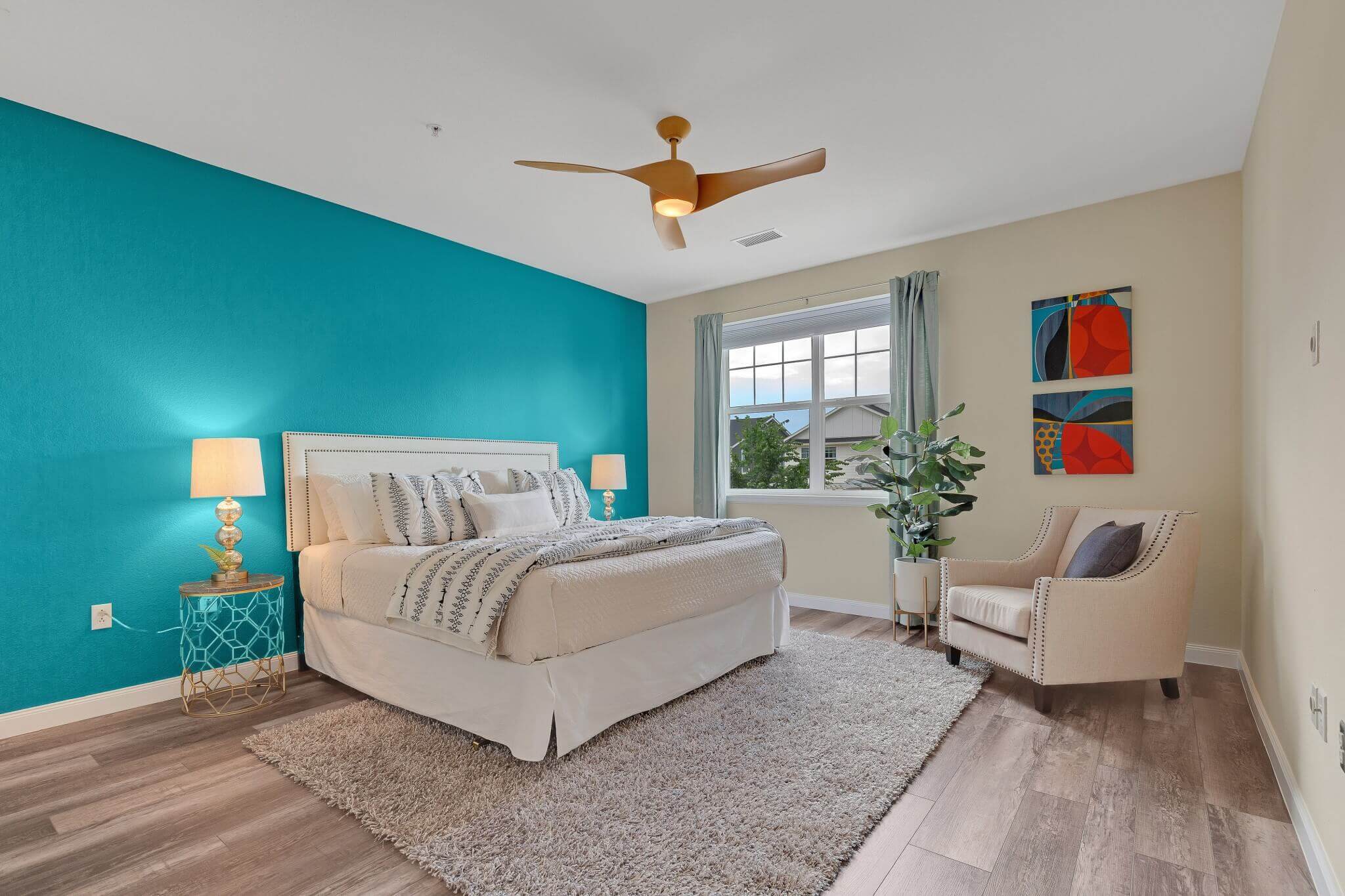 Bedroom with teal and beige walls, wood floor, ceiling fan and window.