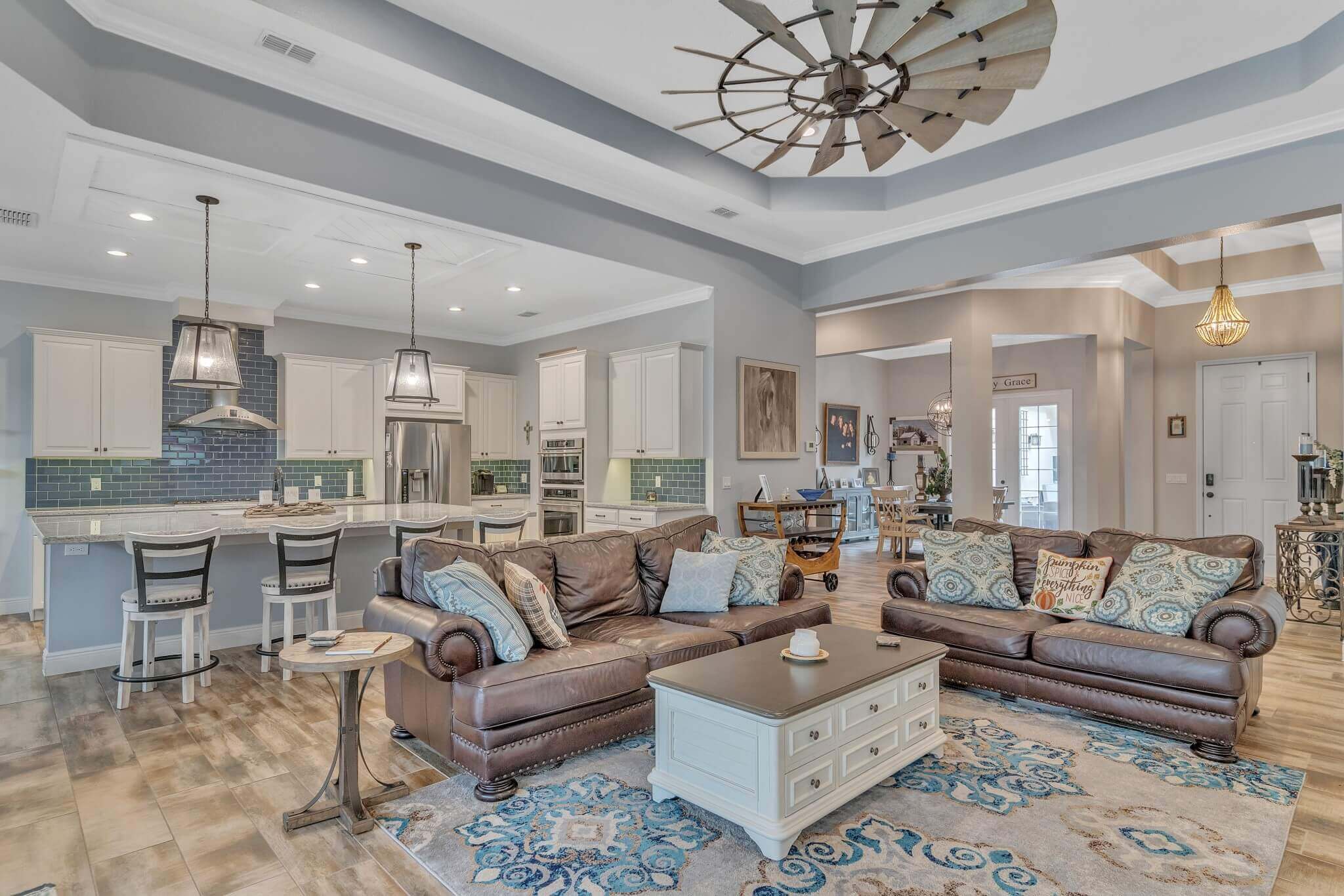 A large living room and kitchen with a wood floor, area rug, sofas, and a windmill for a fan.